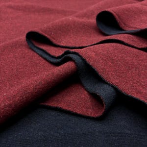 Puede incluir: Primer plano de un textil doblado. La tela tiene un exterior rojo oscuro y un interior azul marino. Los bordes están acabados con un ribete azul marino, creando un contraste. La tela parece suave y texturizada.