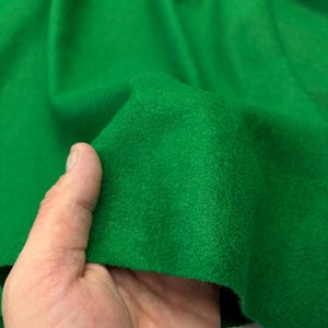 May include: Close-up of a vibrant green fabric. The material is soft and appears to be a felt or similar textile. The texture is visible, with slight variations in the color. The fabric is being held, showing its flexibility and drape.