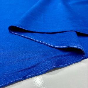 Puede incluir: Primer plano de una tela azul vibrante con un tejido texturizado. Los bordes est&aacute;n acabados con una costura blanca. La tela est&aacute; doblada, creando sombras y resaltando la textura y el color del material.