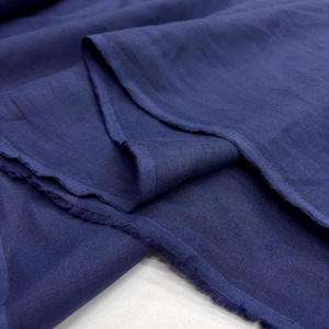 May include: Close-up of a navy blue linen fabric. The fabric is draped and folded, showcasing its texture and the raw edges. The color is a deep, saturated blue, with subtle variations in tone due to the folds and light.