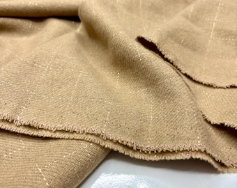 May include: Close-up of tan fabric with a subtle grid pattern and metallic gold threads woven throughout. The edges of the fabric are frayed, revealing a delicate pink thread. The fabric is folded, showing its texture and drape.