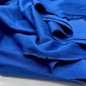 Puede incluir: Primer plano de una tela azul vibrante con textura visible y pliegues sutiles. Los bordes est&aacute;n acabados con una costura blanca. La tela parece ser un material de peso medio, adecuado para proyectos de ropa o decoraci&oacute;n del hogar.