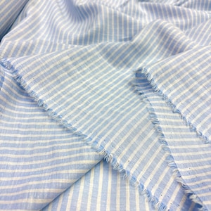 May include: Pale blue and white striped fabric with a fringed edge. The fabric is folded, displaying the texture and pattern. The stripes are evenly spaced and run horizontally across the material.