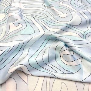 May include: A pale blue fabric with a flowing, wave-like pattern. The design features curved lines in black, white, and shades of blue. The fabric is draped, showing its texture and the interplay of light and shadow.