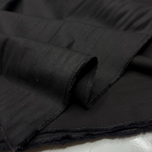 Puede incluir: Primer plano de una tela de color gris oscuro con un tejido texturizado. La tela está doblada, revelando los bordes crudos y sin terminar. El material parece ser un textil de peso medio, adecuado para proyectos de ropa o decoración del hogar.