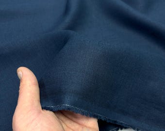 May include: Close-up of a piece of navy blue fabric. The fabric is held in a hand, showing its texture and the raw edge. The material appears to be linen or a similar woven textile, with a slightly irregular surface.