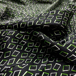 May include: Black fabric featuring a repeating pattern of white and green outlined rectangles. The fabric is draped, creating folds and shadows. The geometric pattern is evenly spaced across the material, adding depth to the design.