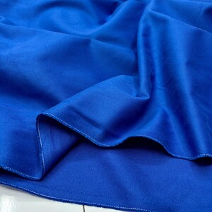 Puede incluir: Primer plano de una tela azul vibrante, mostrando su textura y pliegues. La tela tiene un aspecto liso y es probablemente un material textil. Los bordes de la tela son visibles, con una costura blanca.