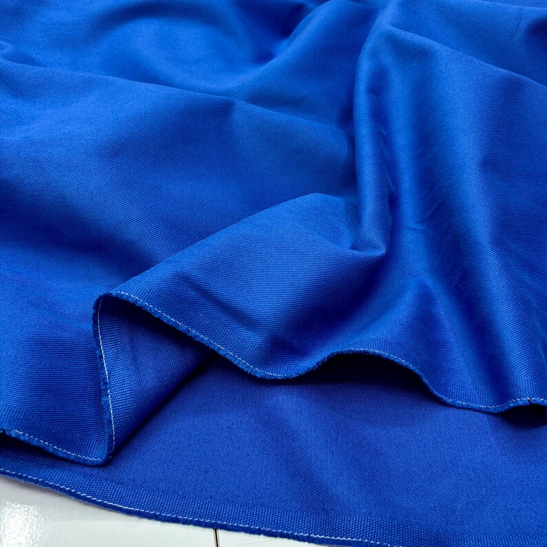 Puede incluir: Primer plano de una tela azul vibrante, mostrando su textura y pliegues. La tela tiene un aspecto liso y es probablemente un material textil. Los bordes de la tela son visibles, con una costura blanca.