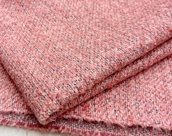 May include: Close-up of a folded piece of pink tweed fabric. The fabric has a textured surface with a mix of pink, gray, and white threads. The edges of the fabric are frayed, revealing the weave.