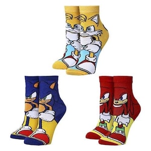 May include: Three pairs of crew socks featuring characters from the Sonic the Hedgehog franchise. One pair is yellow with Tails, another is blue with Sonic, and the third is red with Knuckles. Each sock has a character design on the front.