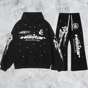 Pode incluir: Conjunto de moletom preto e calças a condizer. O moletom apresenta o texto "Hellstar" em branco, juntamente com gráficos de estrelas e chamas. As calças têm cintura com cordão e o mesmo design de texto e chamas "Hellstar".