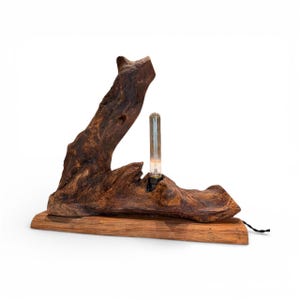 Puede incluir: Lámpara rústica de madera, con base de madera flotante marrón oscuro y una bombilla tubular. La lámpara está montada sobre una base rectangular de madera, con un cable de alimentación negro. Dimensiones: unos 30 cm de largo.