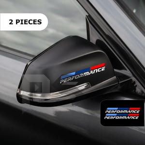 May include: A set of two black car side mirror decals featuring the word PERFORMANCE in white text, accented by a horizontal blue and red stripe design. The stickers are shown applied to a black vehicle side mirror with an integrated turn signal light.