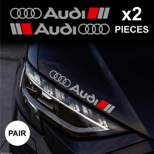 Può includere: Adesivi Audi per auto. Gli adesivi argento e rossi presentano il logo e il testo Audi. L'immagine mostra gli adesivi sul cofano nero di un'auto. È visibile anche il testo "x2 PIECES".