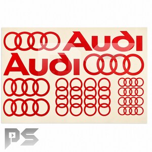 Peut inclure: Une feuille rectangulaire présentant plusieurs logos Audi rouges et des ensembles de quatre anneaux entrelacés. Le design comprend deux grands logos Audi avec leurs anneaux, deux rangées d'anneaux plus grands et deux grilles d'anneaux plus petits.