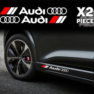 May include: A black car with a silver and black wheel. The car has a white and red Audi logo sticker on the side. The image also shows the text "X2 PIECE" in white.
