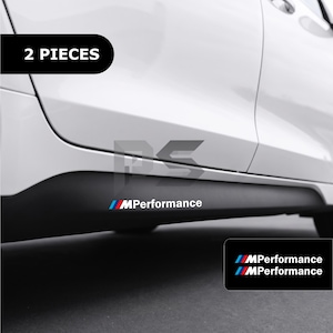 Pode incluir: Um conjunto de dois autocolantes brancos MPerformance com riscas azuis, roxas e vermelhas aplicados no painel lateral preto de um carro branco. O texto 2 PIECES é exibido numa caixa preta no canto superior esquerdo.