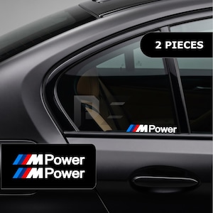 以下が含まれることがあります： 青、紫、赤の斜めストライプと白い「M Power」の文字が特徴的な、車用ウィンドウデカール2枚セット。この粘着ステッカーは、車両のガラス面に貼り付けて使用するように設計されており、すっきりとした外観を提供します。