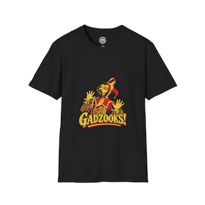 May include: A black short-sleeved t-shirt featuring a graphic print of a jester in a red and yellow costume with hands raised. Below the jester, the word GADZOOKS! is printed in bold yellow letters with a red outline on the front of the shirt.
