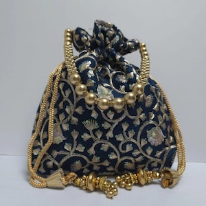 Könnte beinhalten: Marineblaue Kordelzugtasche mit goldener Blumenstickerei und goldenen Perlenakzenten. Die Tasche hat einen Kordelzugverschluss und goldene Seilgriffe. Goldene Quasten verzieren den Boden. Ein kleiner, dekorativer Beutel.