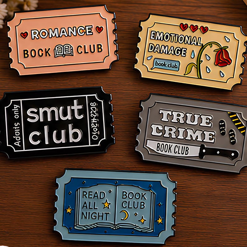 May include: Five rectangular enamel pins shaped like movie tickets. The pins feature text and illustrations: ROMANCE BOOK CLUB with hearts, EMOTIONAL DAMAGE with a rose, smut club with adults only, TRUE CRIME BOOK CLUB with a knife, and READ ALL NIGHT BOOK CLUB with an open book and stars.