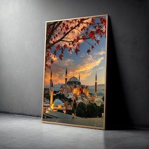 Puede incluir: Una impresión enmarcada de Santa Sofía en Estambul, Turquía, al atardecer. La imagen presenta la icónica mezquita con sus cúpulas y minaretes, sobre un cielo colorido. Hojas rojas de otoño enmarcan la parte superior de la imagen.