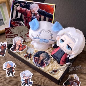 Könnte beinhalten: Eine Sammlung von Devil May Cry-Fanartikeln, bestehend aus einer Plüschfigur mit weißem Haar, einem weißen Plüschhund mit blauen Ohren, einem runden Ansteckbutton, einer silberfarbenen Anhängerkette und mehreren illustrierten Aufklebern mit Dante.