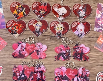 Puede incluir: Una colección de llaveros acrílicos en forma de corazón con personajes de Hazbin Hotel. La fila superior muestra retratos individuales sobre fondos rojos, mientras que las filas inferiores presentan parejas con textos como Love You, Miss You, F*** Me y Be Mine.