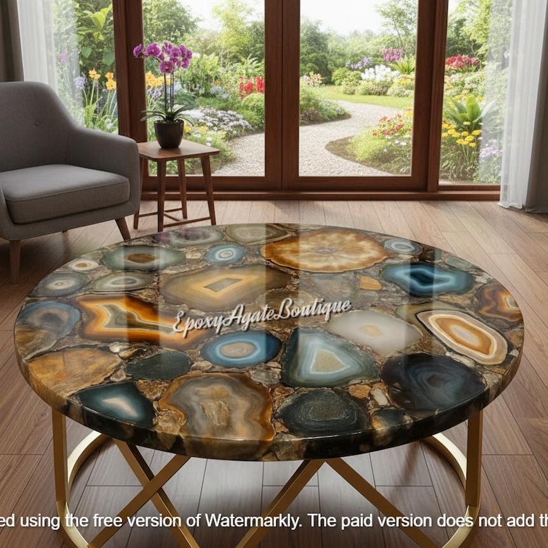May include: A round coffee table with a unique agate stone top. The table features a gold metal base and a colorful mosaic of agate slices in shades of blue, brown, and gold. The text "Epoxy Agate Boutique" is visible on the table.