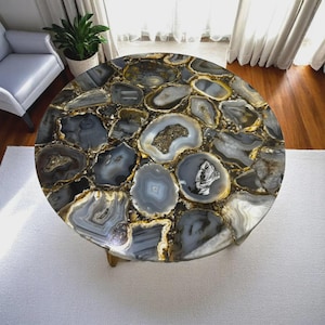 May include: A circular coffee table featuring a top crafted from polished agate slices in grey, white, and gold hues. The table has a natural, organic aesthetic and rests on a light-coloured base. The table is approximately 100 cm in diameter.