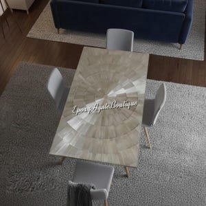 Könnte beinhalten: Ein rechteckiger Esstisch mit hellem, radialem Design, umgeben von vier grauen Stühlen. Der Tisch hat Holzbeine und steht auf einem grauen Teppich. Im Hintergrund ist ein marineblaues Sofa zu sehen. Der Text "Epoxy Agate Boutique" befindet sich auf dem Tisch.