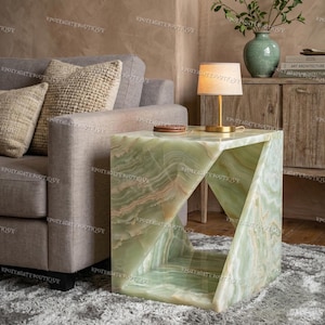 Könnte beinhalten: Ein grüner Onyx-Beistelltisch mit einem einzigartigen geometrischen Design. Der Tisch hat eine Würfelform mit einem dreieckigen Ausschnitt auf einer Seite. Er steht neben einem grauen Sofa und einem Teppich.