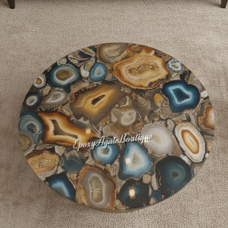 May include: Round coffee table with a unique agate stone top. The table features a mosaic of agate slices in shades of brown, gold, blue, and white. The surface has a polished finish, and the table is suitable for a living room or lounge area.