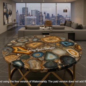 May include: A round coffee table with a unique agate stone top. The table features a gold-colored metal base and a mosaic of colorful agate slices in shades of blue, brown, and gold. The text "Epoxy Agate Boutique" is visible on the table.
