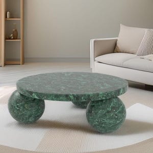 May include: A circular coffee table with a green marble top and three spherical legs. The table is approximately 91 cm in diameter. A modern design element for a living room.