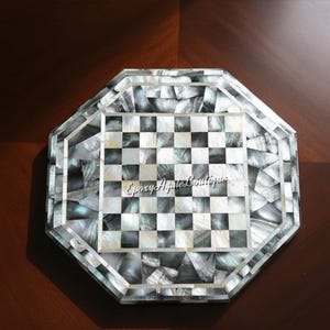 May include: An octagonal chess board with a mother-of-pearl inlay. The playing surface features a classic black and white checkered pattern. The border is made of iridescent pieces. The text "Epoxy Agate Boutique" is visible on the board.