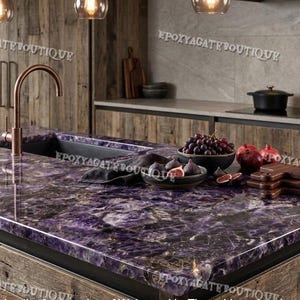 Può includere: Un'isola cucina con un piano di lavoro viola e bianco. Il piano di lavoro ha un lavandino integrato e un rubinetto in rame. L'isola è in legno e ha un aspetto rustico. Ci sono ciotole di frutta e taglieri sul piano di lavoro.