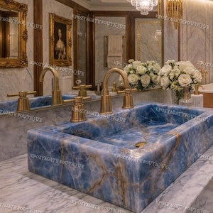 Puede incluir: Un lavabo rectangular de mármol azul con grifos dorados es el punto focal de este lujoso baño. Las vetas del lavabo presentan tonos marrones y blancos. El baño también incluye un espejo, obras de arte enmarcadas y una bañera color cobre.