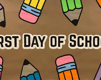 Puede incluir: Fondo marrón con el texto "FIRST DAY OF SCHOOL!" en letras blancas en negrita con contorno negro. Lápices de colores morados, amarillos, verdes, azules y naranjas están dispersos alrededor del texto.