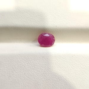 Op de afbeelding: Een losse, ovaalvormige edelsteen met een gefacetteerd oppervlak en een diepe, levendige magenta-roze kleur. De steen heeft een gepolijste afwerking met meerdere geometrische facetten die het licht over het oppervlak reflecteren.