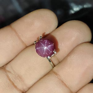 Op de afbeelding: Een zilveren ring met een ronde, in cabochon geslepen sterrobijn. De diep magenta gekleurde steen vertoont een duidelijk zespuntig sterpatroon op het oppervlak en wordt vastgehouden door een eenvoudige zetting met vier pootjes op een dunne zilveren ring.