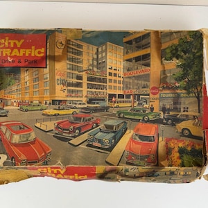 Op de afbeelding: Vintage speelgoeddoos "City Traffic Drive & Park". De doos heeft een kleurrijke illustratie van een stadsgezicht met auto's, gebouwen en de tekst "City Traffic Drive & Park". De doos is gemaakt van karton en vertoont tekenen van slijtage.