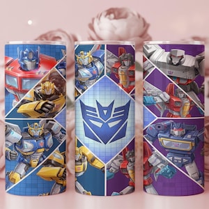 May include: Three cylindrical tumblers featuring Transformers characters. The tumblers showcase Optimus Prime, Bumblebee, and other Autobots and Decepticons in a geometric design. The center tumbler displays the Decepticon logo. The background is a soft pink.