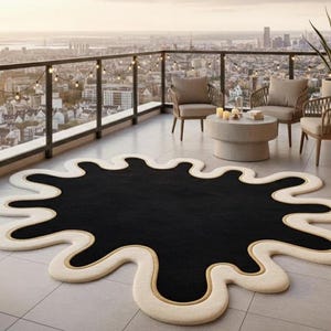 Puede incluir: Una alfombra de forma abstracta con un centro negro y un borde color crema. La alfombra tiene un acento dorado a lo largo del borde y est&aacute; colocada en un patio embaldosado. El entorno exterior incluye asientos y vistas a la ciudad.