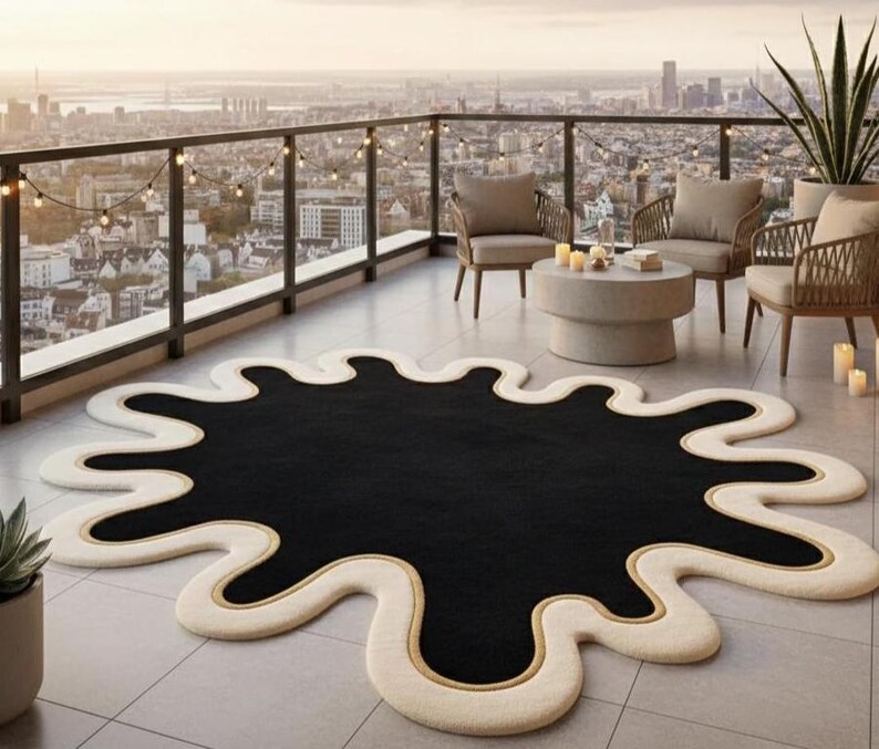 Puede incluir: Una alfombra de forma abstracta con un centro negro y un borde color crema. La alfombra tiene un acento dorado a lo largo del borde y est&aacute; colocada en un patio embaldosado. El entorno exterior incluye asientos y vistas a la ciudad.
