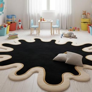 Puede incluir: Una alfombra negra grande con una forma irregular que se asemeja a una mancha de tinta. La alfombra tiene un borde color crema con un fino acento dorado. Dos almohadas grises descansan sobre la alfombra en una habitaci&oacute;n infantil.