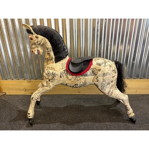 May include: A decorative horse sculpture with a newspaper print design. The horse has a black mane and tail, red eyes, and a black saddle with red trim. The sculpture is made of a light-coloured material.