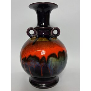 May include: A ceramic vase with a rounded body and a flared top. The vase displays a vibrant colour scheme, with a gradient of red, orange, and dark purple tones. It has two loop handles and a pedestal base, standing approximately 30 cm tall.