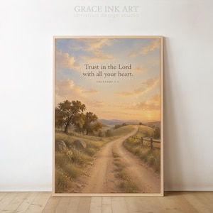 Op de afbeelding: Een rechthoekige wandkunstprint in een lichthouten lijst met een landschapsschilderij van een zandpad dat bij zonsondergang door grasheuvels slingert. De tekst luidt: Trust in the Lord with all your heart. PROVERBS 3:5. De lucht is gevuld met zachte wolken.
